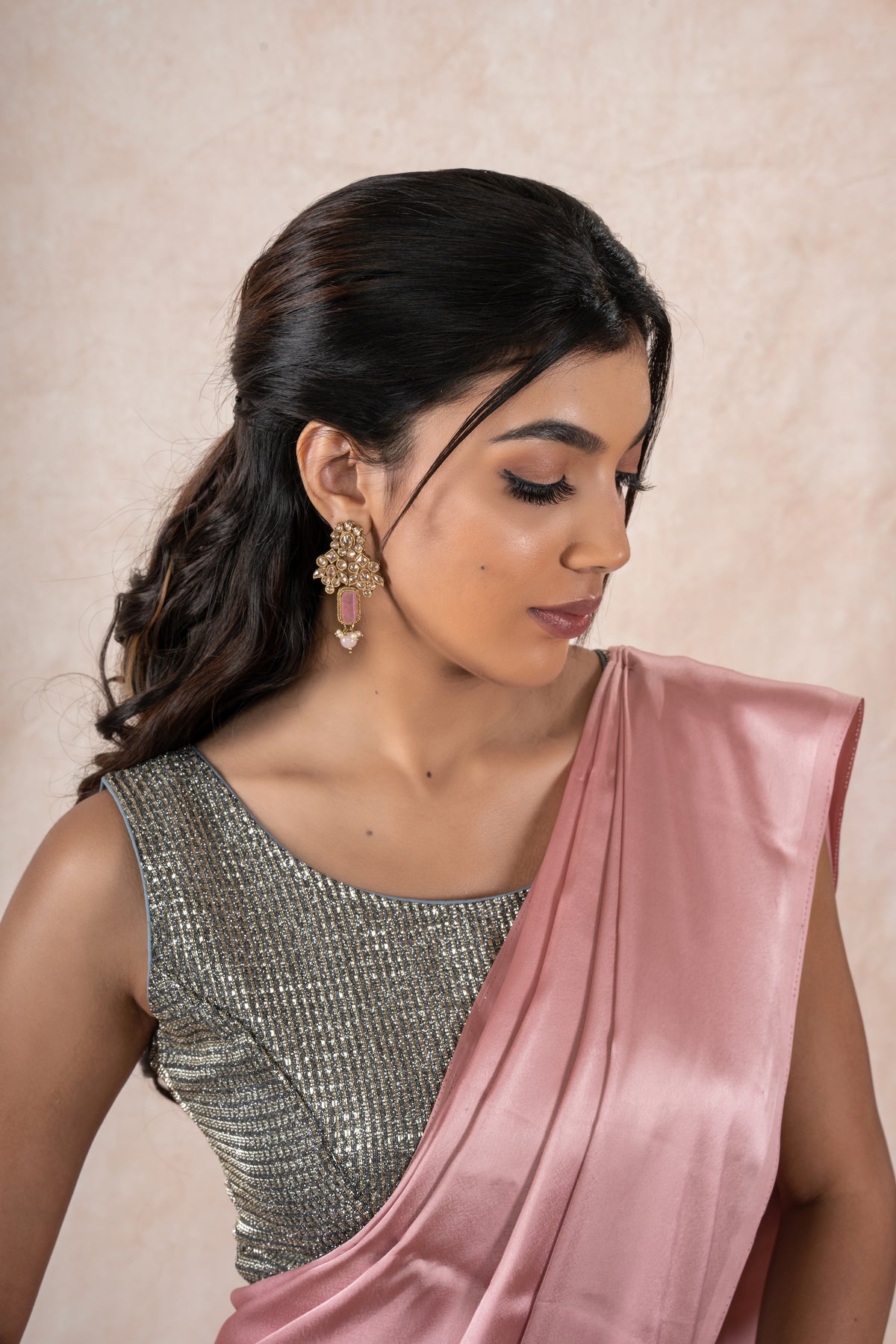 A model draped in a light pink satin silk saree, grey glitter blouse and light pink shaper. The saree is pleated beautifully around the shoulder.