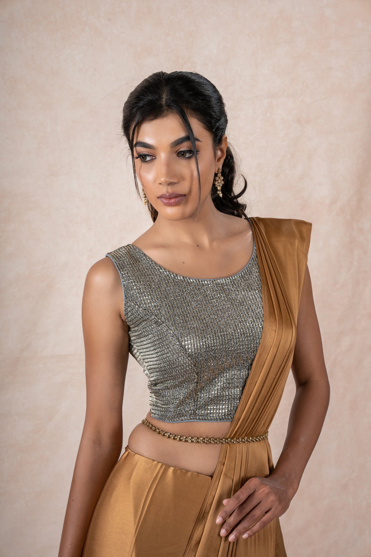 A model draped in a copper brown satin silk saree, grey shimmer blouse and gold buff saree shaper. The saree is pleated and  held with a waist chain.