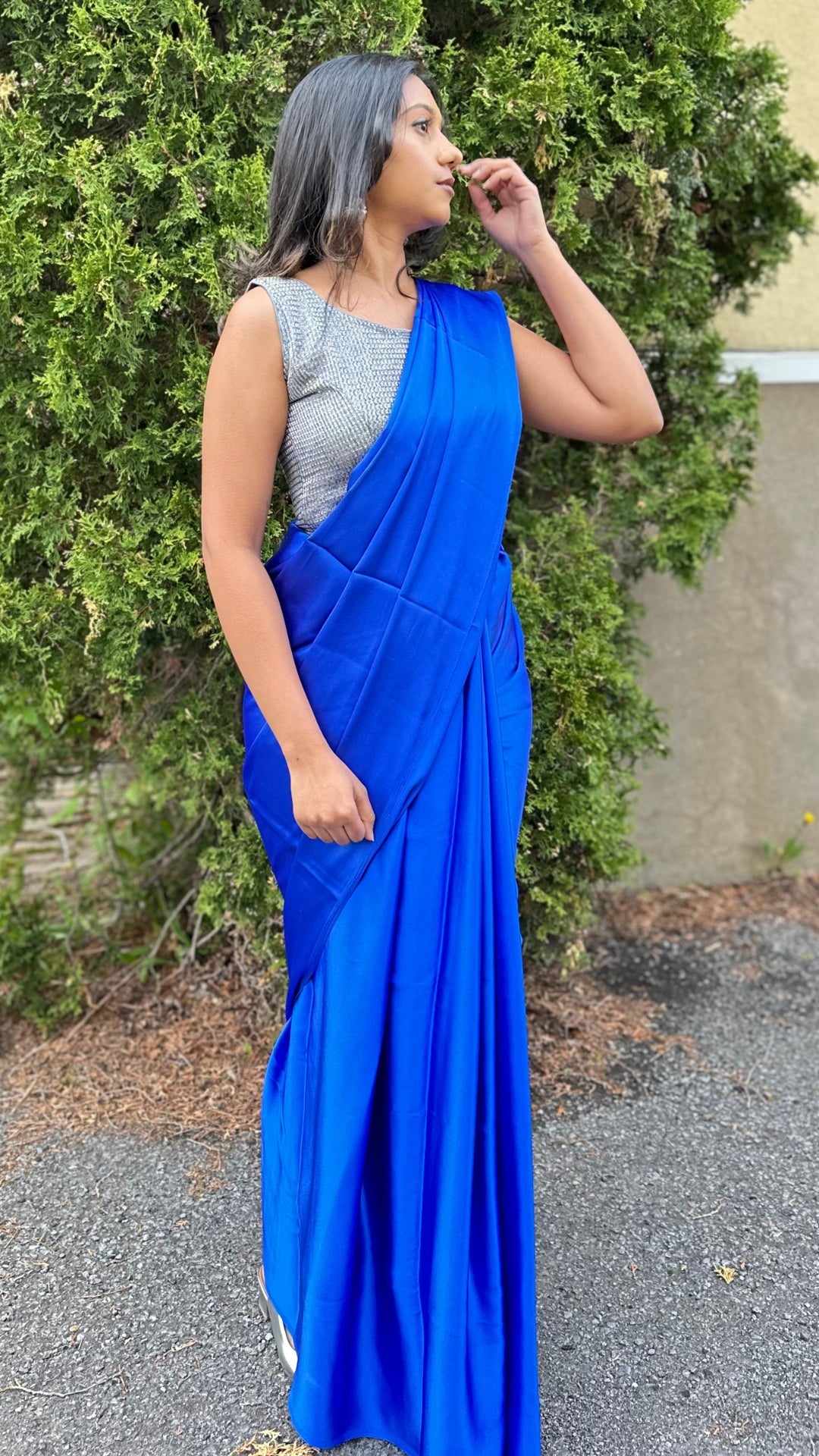 A model draped in a dark blue satin silk saree, grey glitter blouse and dark blue saree shaper. The saree is pleated beautifully around the shoulder.