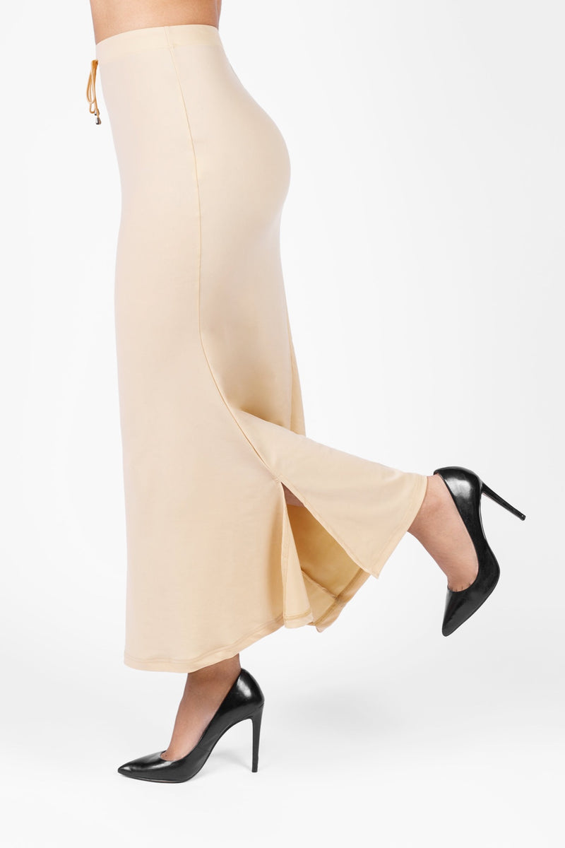 A model wearing Le Pleat's beige/nude/cream color saree shapewear petticoat designed with elastic waistband, drawstring at waist and flare at bottom to drape the sarees.