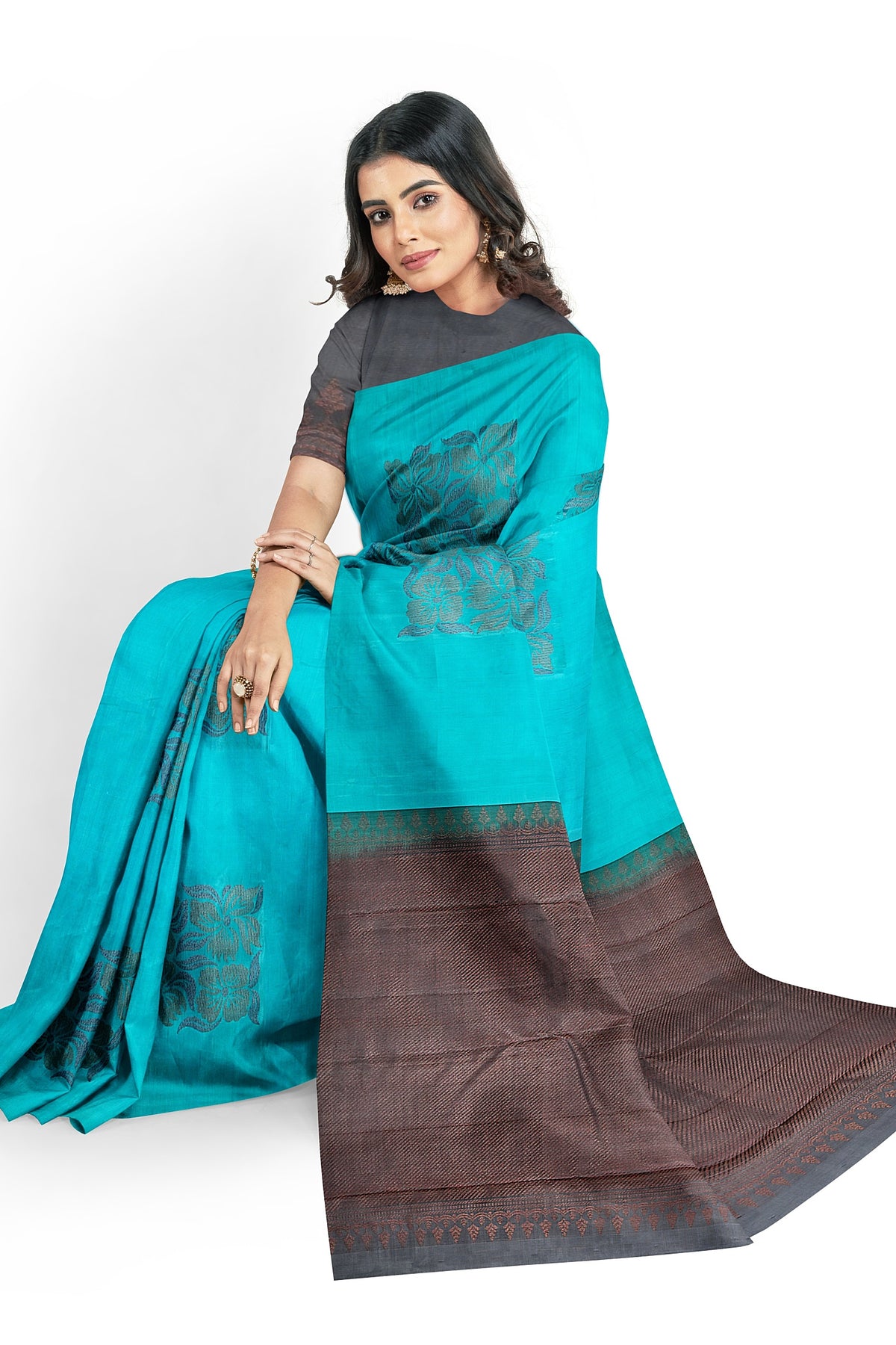 A model draped in a sky blue soft silk handloom saree with blue body and copper brown pallu. The saree is designed with floral motifs in neem zari works. The saree comes with an attached running blouse.